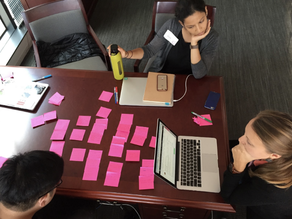 Two Navanauts are sitting at a table looking at a laptop computer and pink sticky notes.
